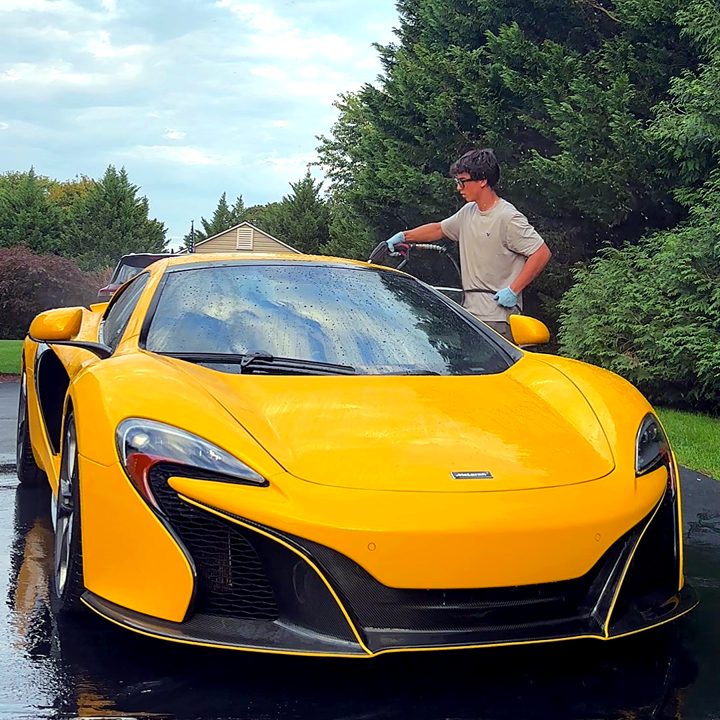 Tanner pressure washing a yellow McLaren 650S in a customer's driveway.