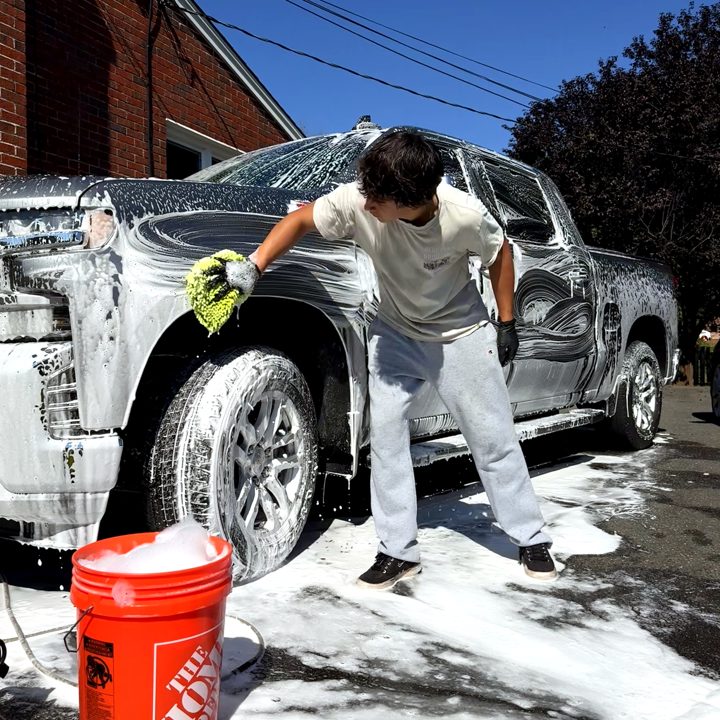 Tanner hand washing a foam-covered pickup in a customer's driveway.