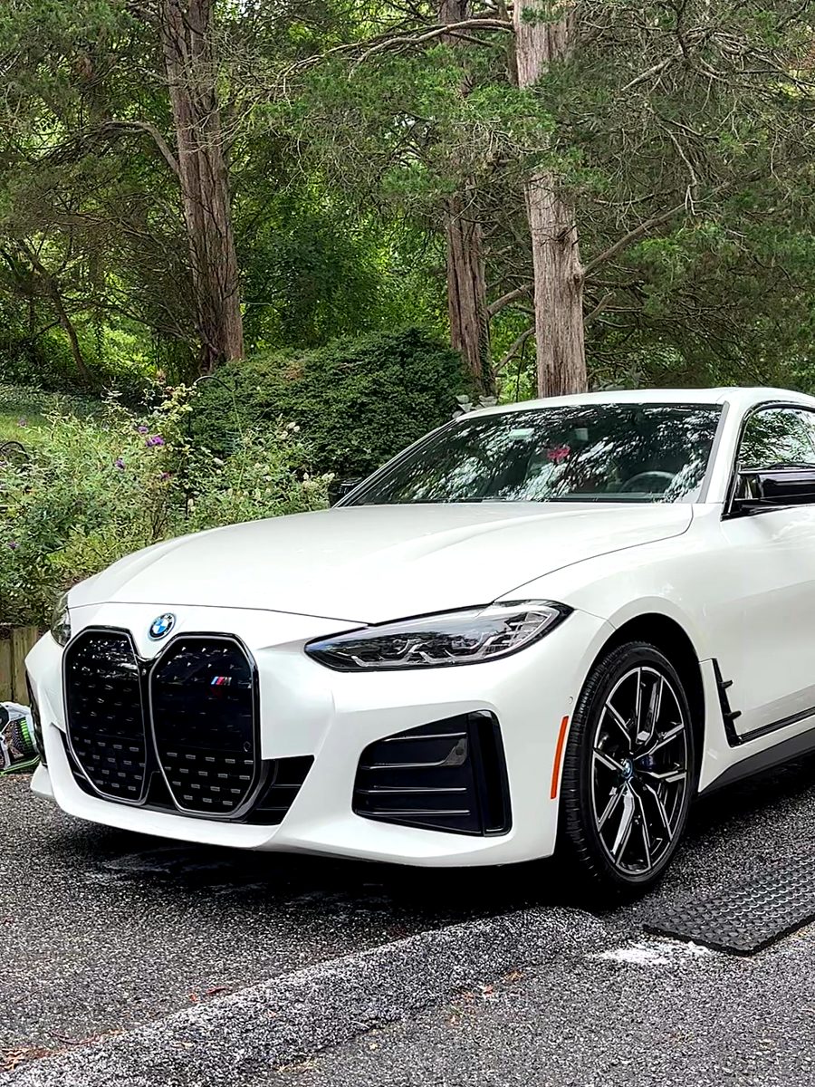 White BMW i4 M50 after an exterior detail in a wooded driveway.