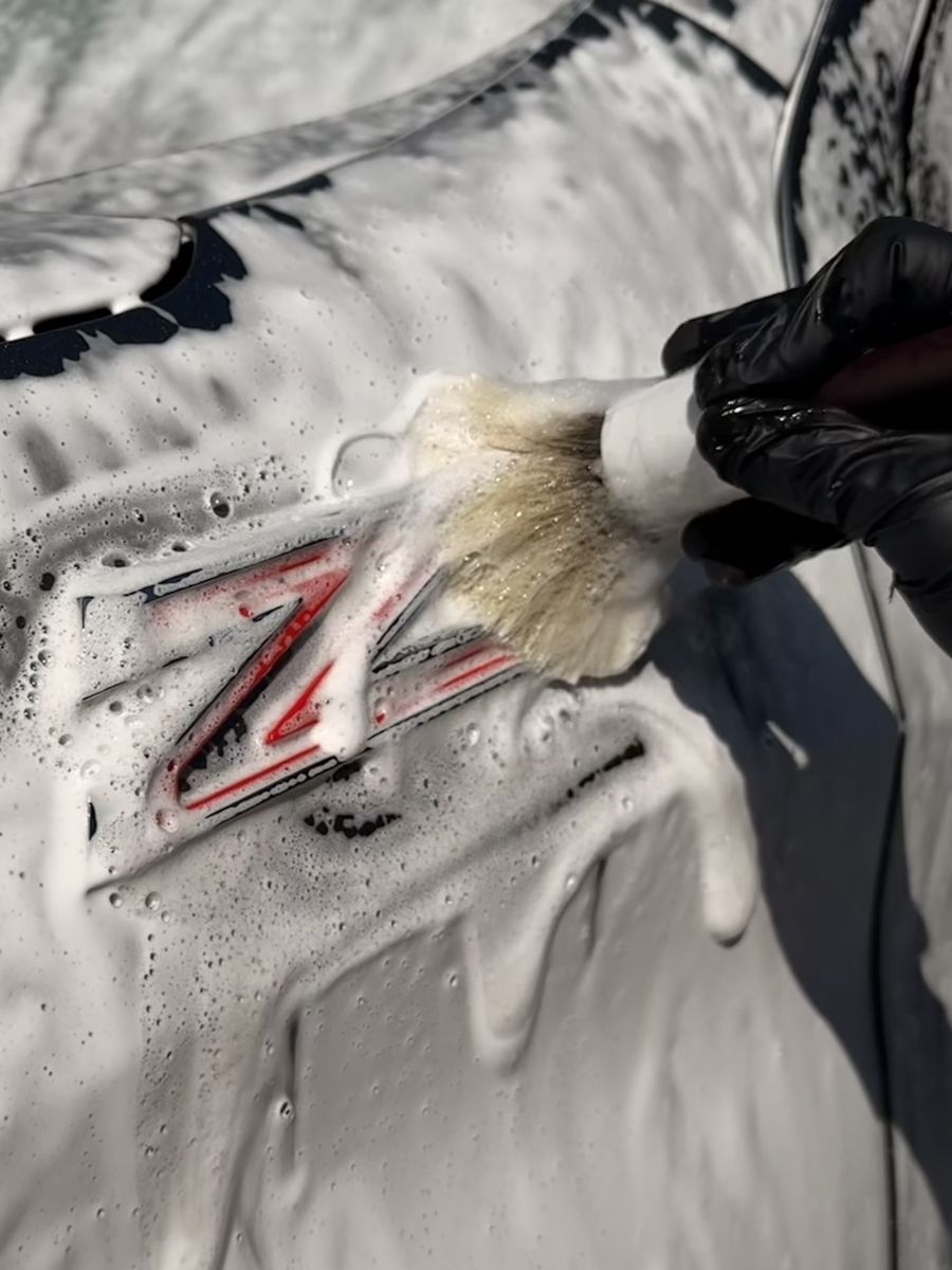 Soft detailing brush cleaning the Z06 badge on a foam-covered Corvette.