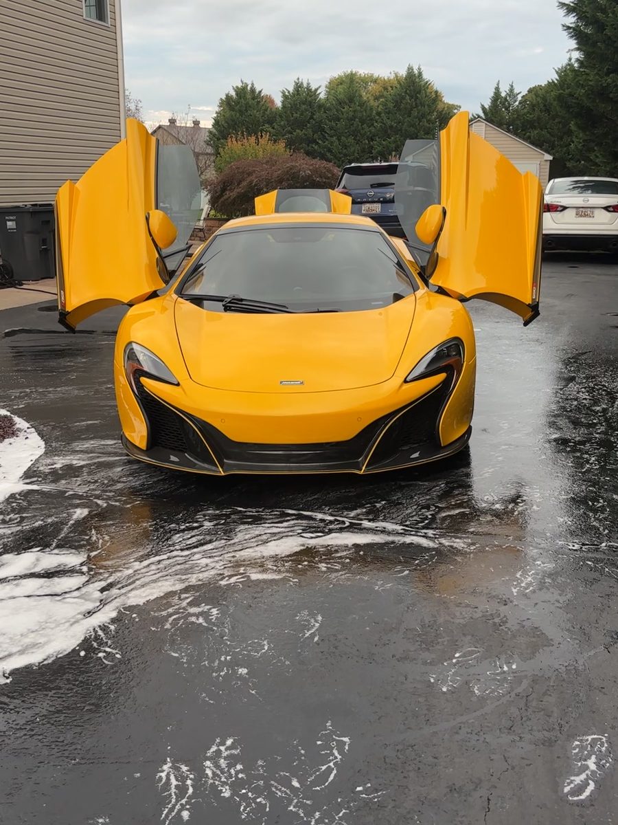 Yellow McLaren 650S with its doors up during a mobile detail, seen from above.